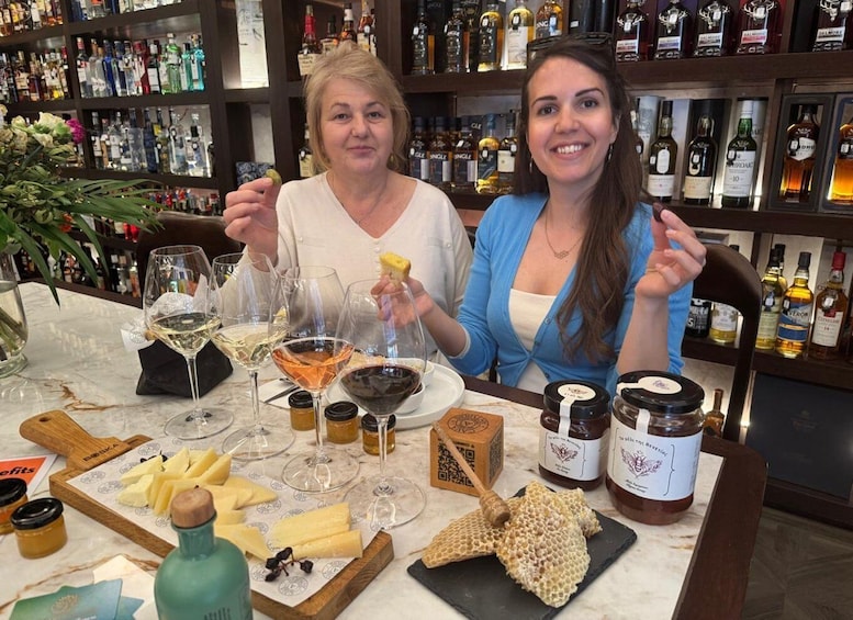 Two people at a bar with wine glasses, cheese, honey, and honey jars. 2