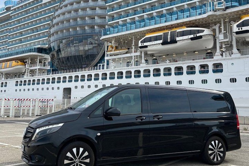 A black minivan parked in front of a large cruise ship with multiple decks and balconies. 2