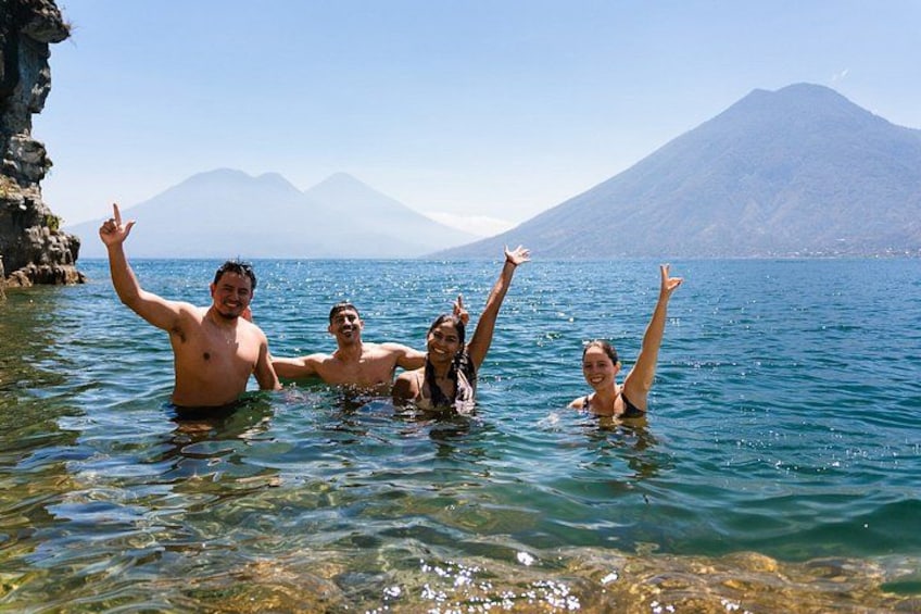 People swimming in clear water with a mountain in the background. 1