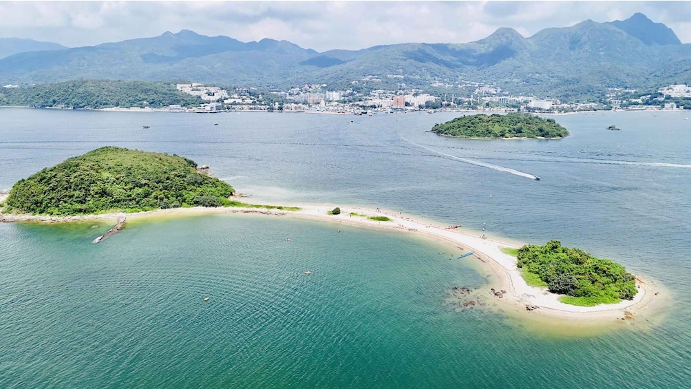 A coastal landscape with a sandy beach, a small island with dense greenery, and a backdrop of mountains. 1