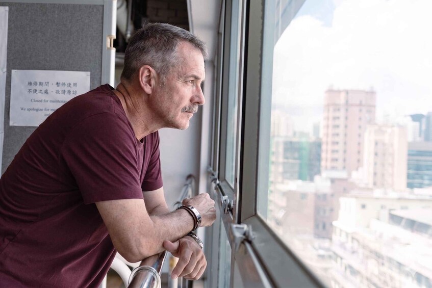 A man leaning on a window sill, looking out at a cityscape. 2