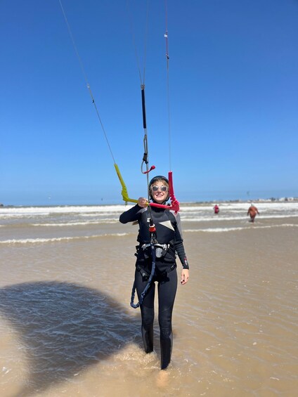 A person in a wetsuit walking on a beach with a kiteboard. 2