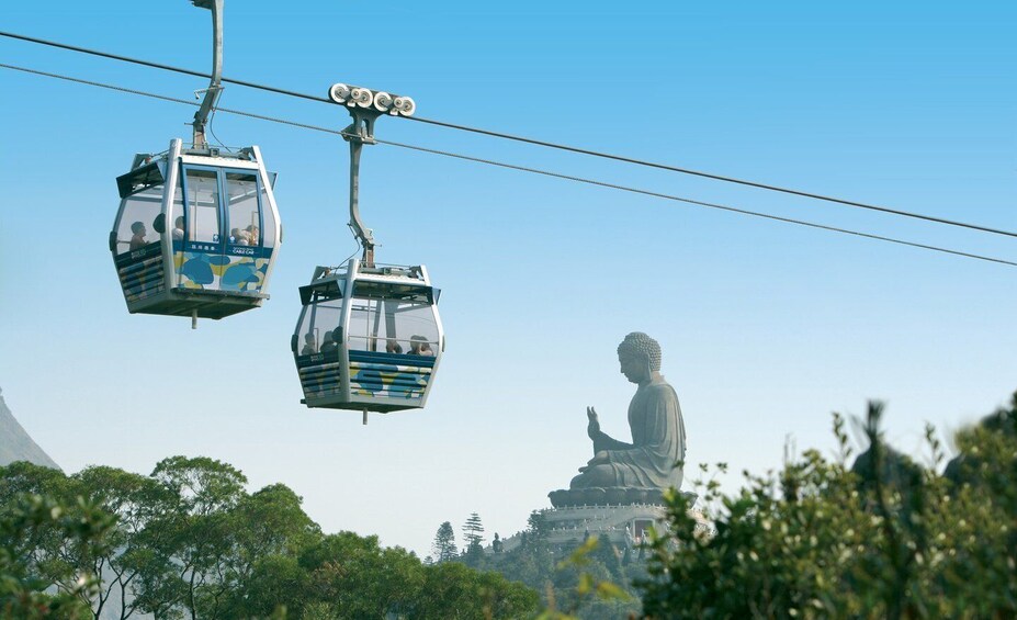 A cable car system with passengers, a large Buddha statue, and lush greenery in the foreground. 1