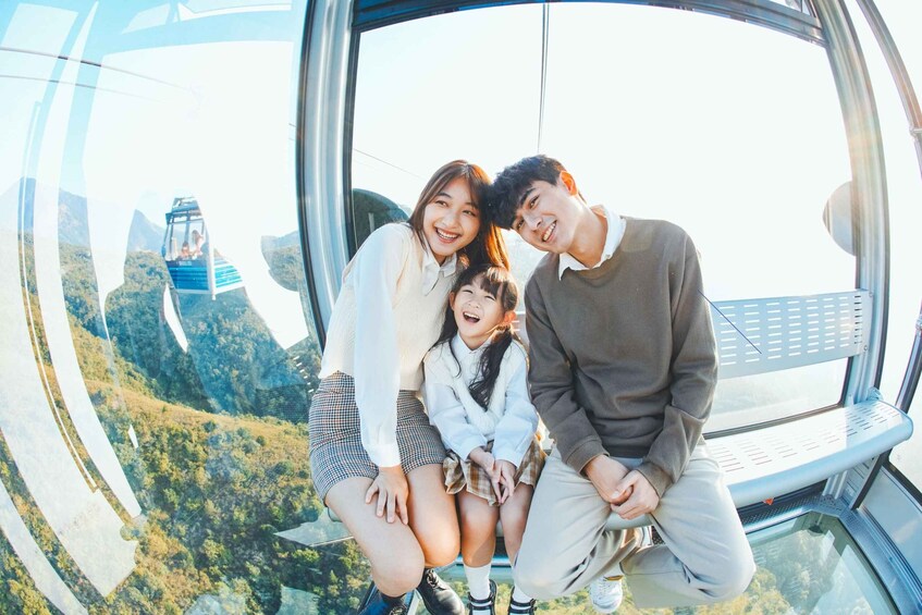 A family on a glass-bottomed cable car with a scenic view of a forested mountain area. 5