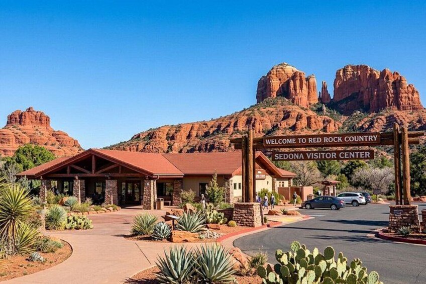 A visitor center with a red rock backdrop, a clear sky, and cacti in the foreground. 1