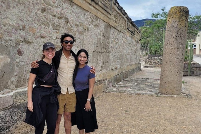 Tres personas de pie frente a un muro de piedra con un alto pilar. 4