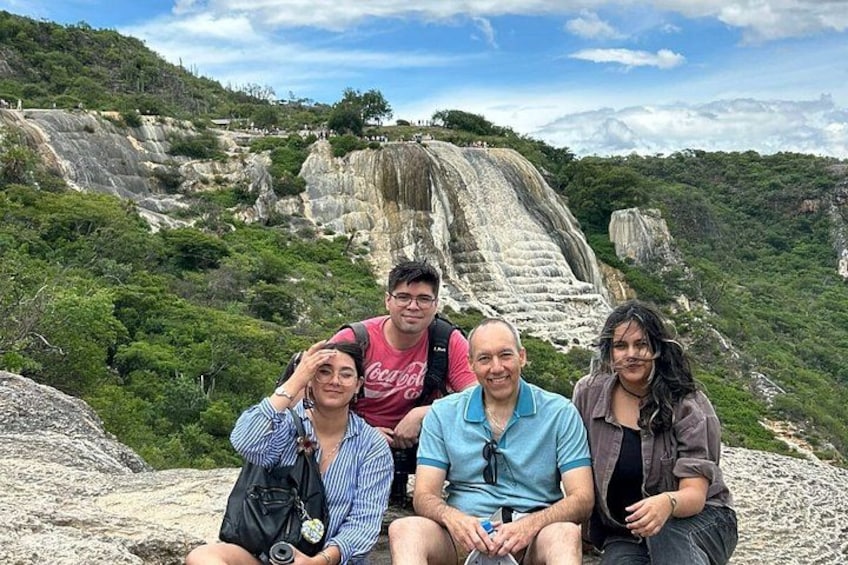 Un grupo de personas sentadas sobre una roca, con una cascada al fondo. 1