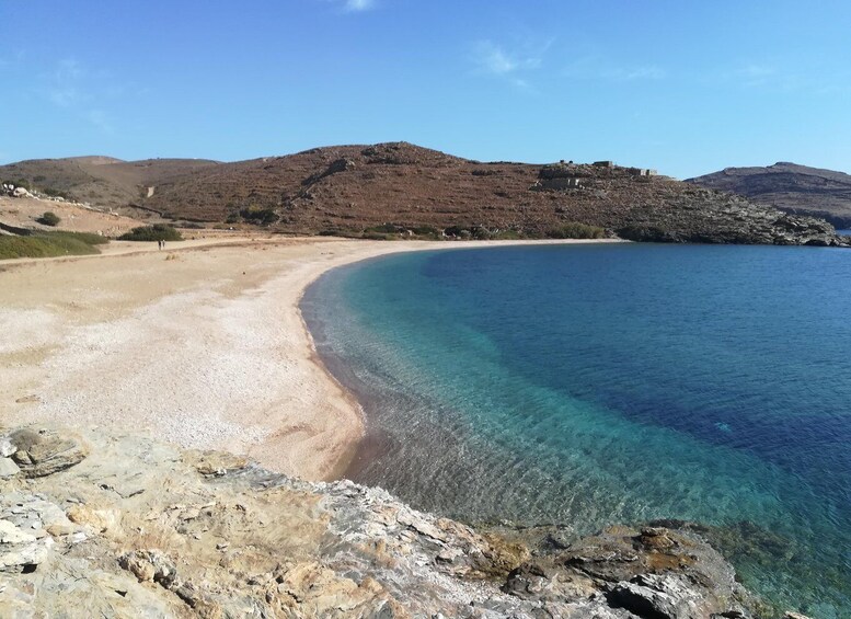 A clear coastal beach with rocky outcrops and a hilly landscape in the background. 2