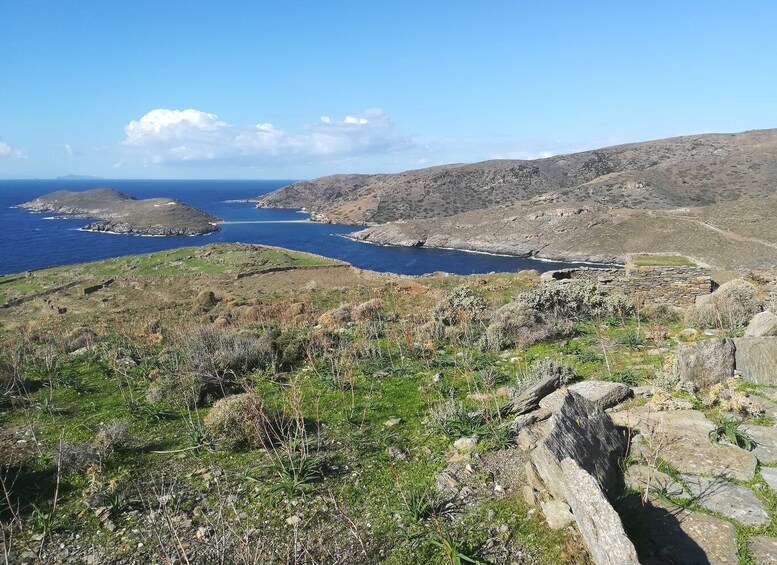 A coastal landscape with rocky terrain, a clear blue sea, and a distant island. 1