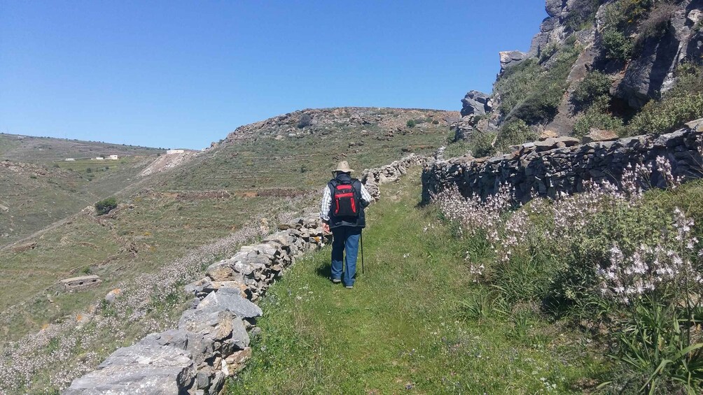 A hiker on a rocky trail with a stone wall on one side and a grassy hillside on the other. 5