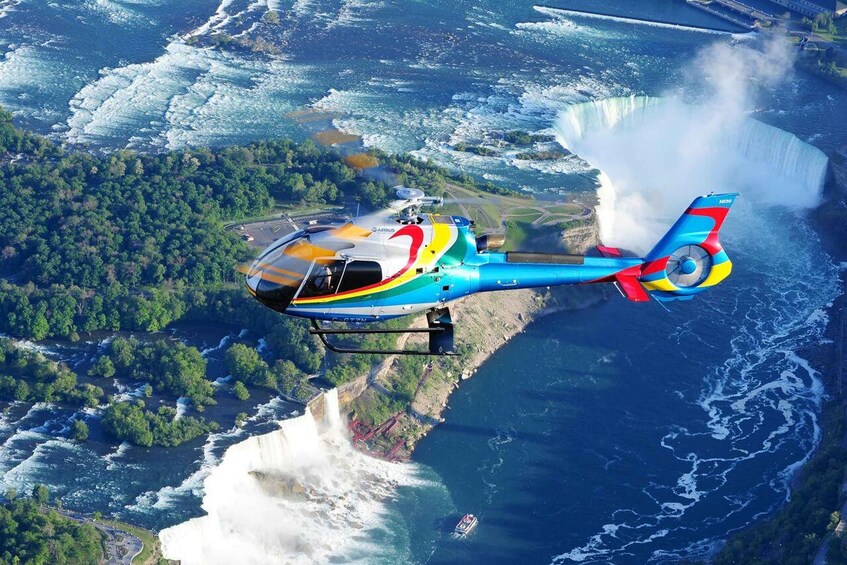 A colorful helicopter flying over a waterfall with a forested landscape below. 4