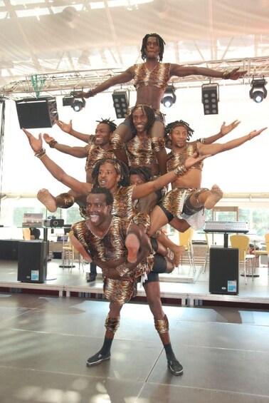 A group of people in matching tiger-striped outfits performing an acrobatic stunt on a stage with lighting equipment and speakers in the background. 5