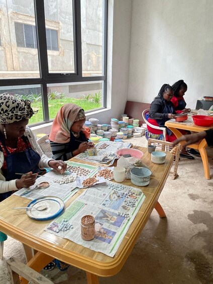 A group of women engaged in pottery making, with clay and pottery tools spread across a table. 2