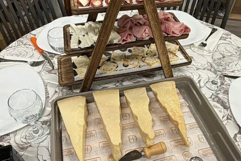 A table with plates, a tray of cheese, and a wooden stand with meat. 4