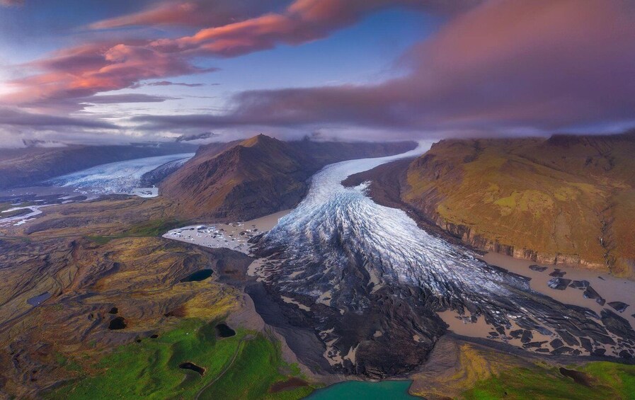 A glacier flowing through a mountainous landscape with green valleys and a river. 2