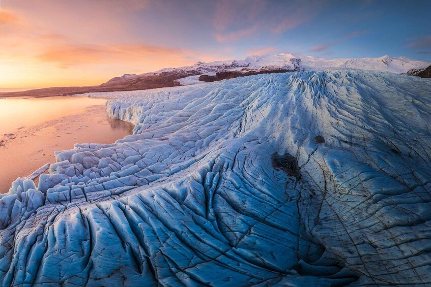 A glacier with a smooth, icy surface and a calm body of water in the foreground. 4