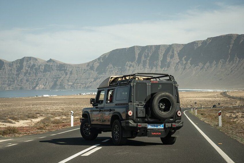 Een zwarte terreinwagen op een verharde weg, met bergen op de achtergrond. 1