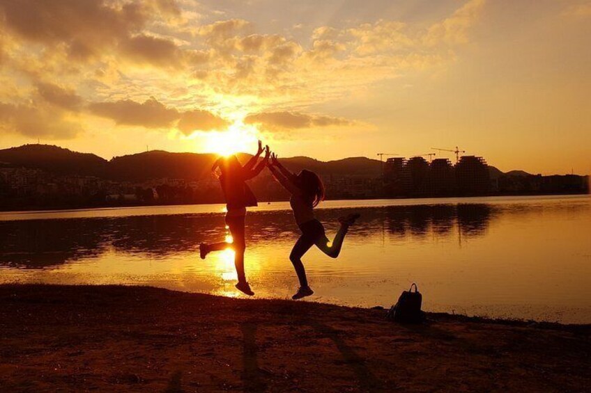 A person standing by a body of water with the sun setting in the background. 4