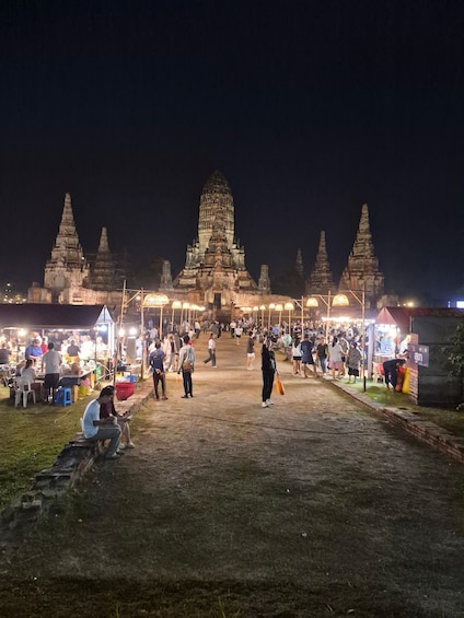 A night scene at a temple complex with multiple towers, a crowd of people, and illuminated stalls. 2