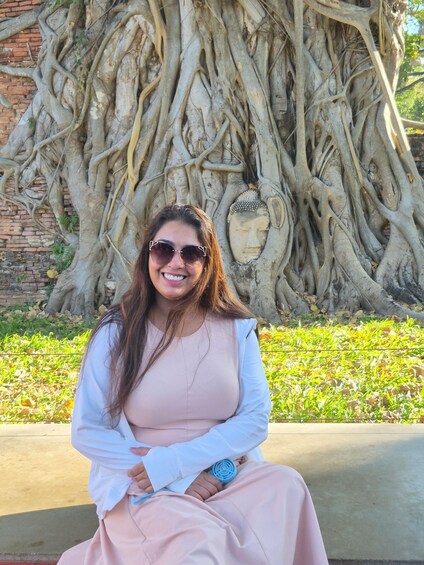 A person sitting in front of a large tree with extensive roots and a Buddha statue. 3
