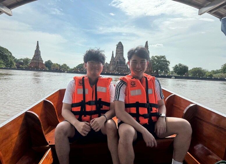Two individuals in a wooden boat wearing orange life jackets, with temple structures in the background. 4