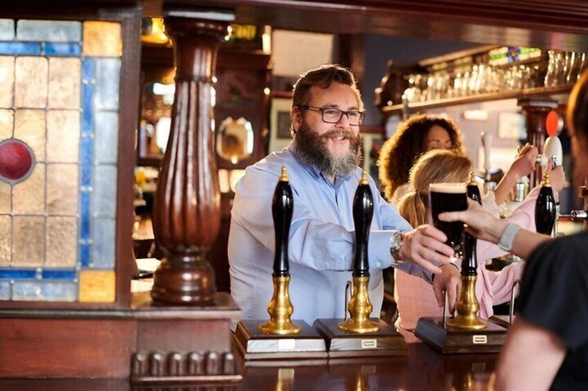 Un bar con un hombre sirviendo cerveza, un vitral y muebles de madera. 4