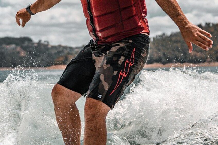 Una persona surfeando una ola con chaleco salvavidas rojo y pantalones cortos de camuflaje. 3