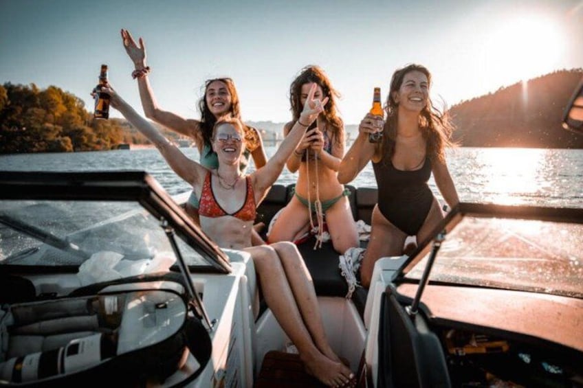 Tres personas en un barco, sosteniendo bebidas, con un cuerpo de agua y un atardecer de fondo. 1