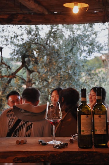A group of people at a wine tasting event with wine bottles and a glass on a wooden table. 5