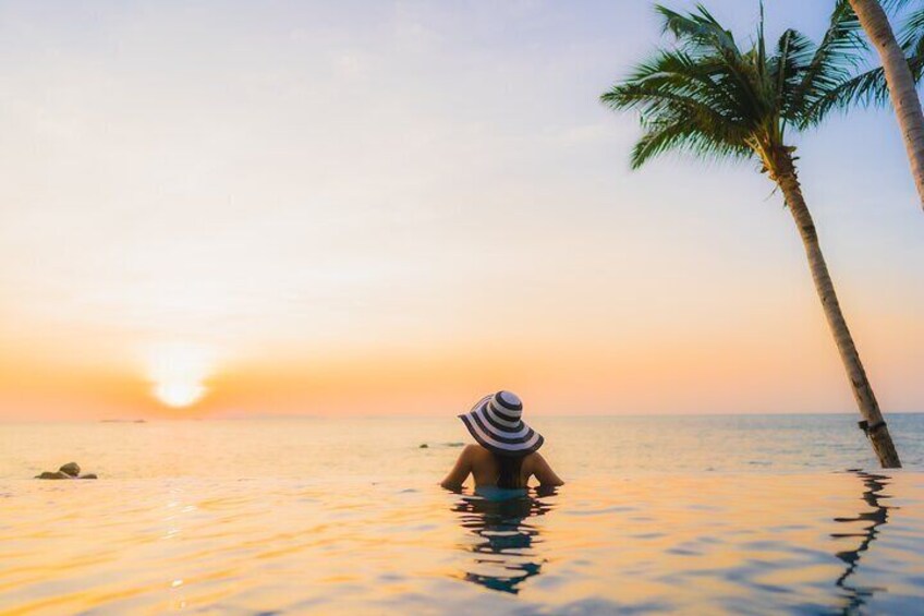 Una persona en una piscina al atardecer, con una palmera y el océano al fondo. 4
