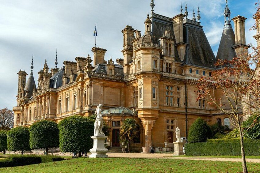 A grand historic building with ornate architecture, a well-maintained garden, and a statue in the foreground. 1