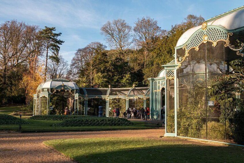 A glasshouse with ornate metalwork, surrounded by manicured lawns and trees. 3