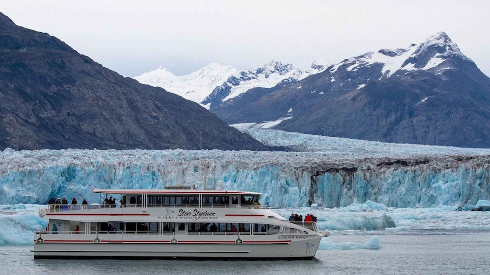 A cruise ship named 'Glacier Spirit' with passengers on deck, sailing past a glacier with mountains in the background. 1