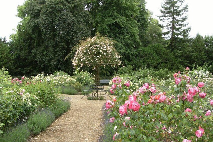 Un jardín con un camino de grava, rosas rosadas y un pabellón. 2