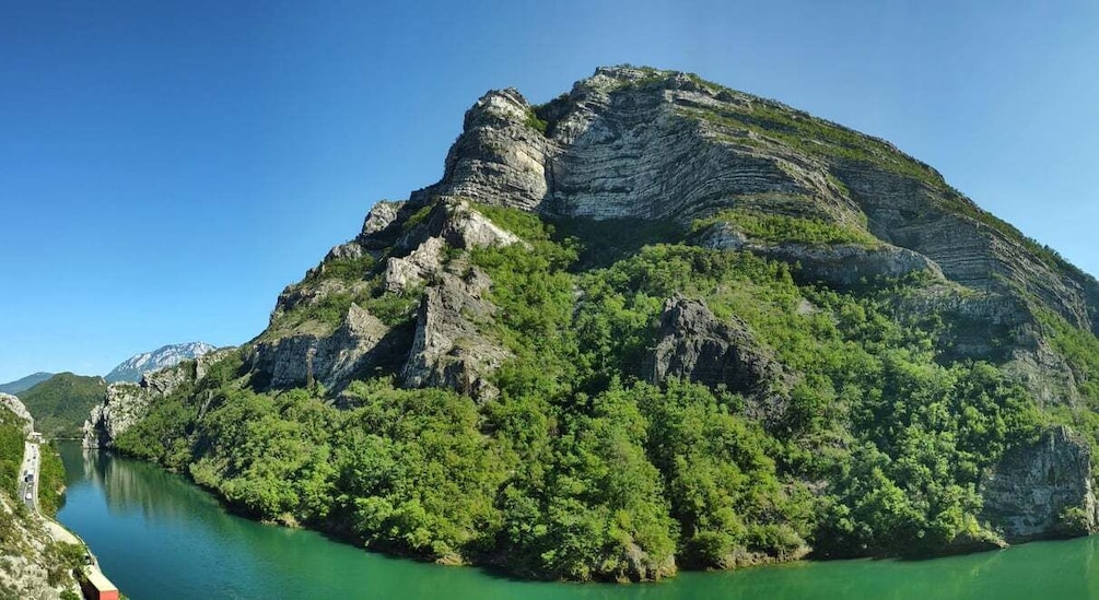 A mountainous landscape with a river, dense greenery, and a clear sky. 1