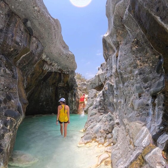 A person walking through a narrow rocky passage with clear water. 4