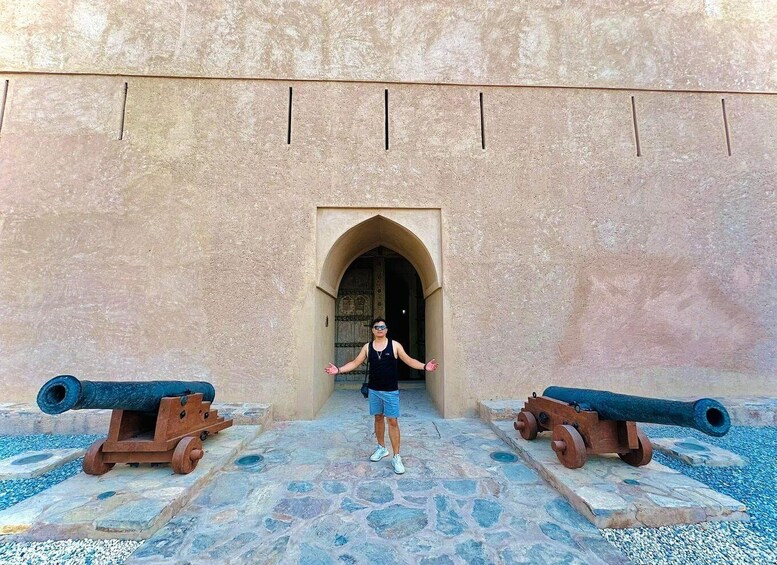 A person standing between two cannons in front of a building with an arched entrance. 3