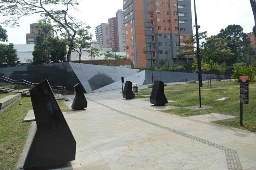 Un sendero con esculturas negras de gran tamaño, un área verde y un edificio al fondo. 3