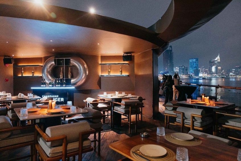 A restaurant with tables set for dining, a champagne bar, and a view of a city skyline at night. 5