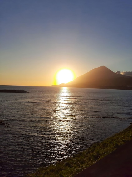 A sunset over a calm sea with a mountain in the background. 1