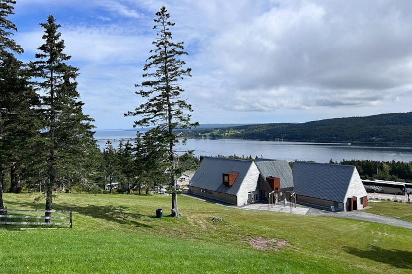 A coastal house with a grassy lawn, two large trees, and a view of the sea. 1