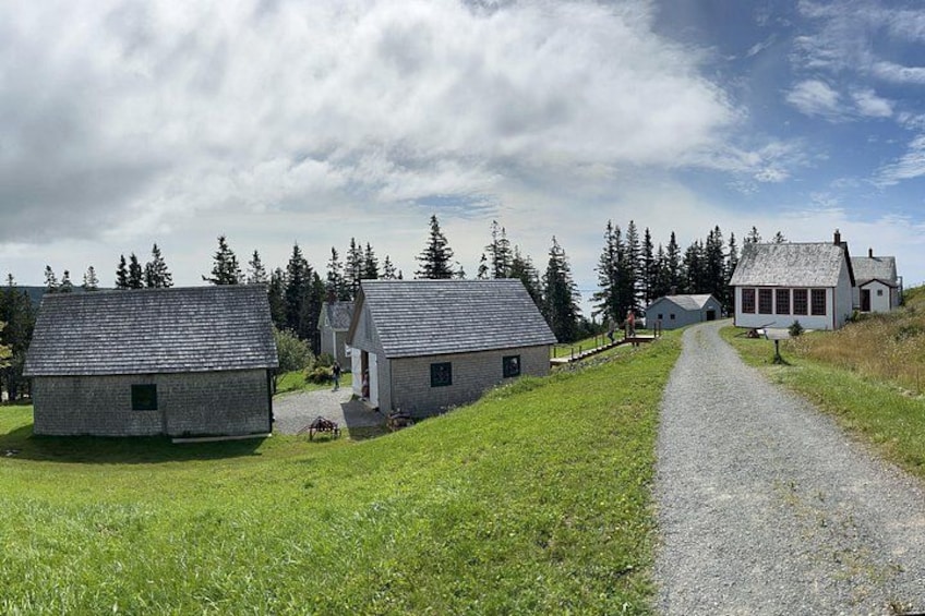 A gravel path leading to a cluster of stone buildings in a rural setting with trees in the background. 2