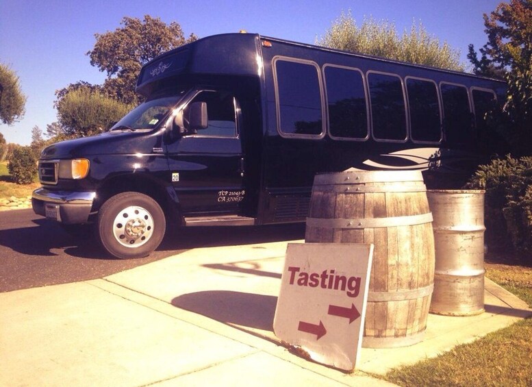 A black van parked on a sidewalk with a sign reading 'Tasting' and two barrels nearby. 1