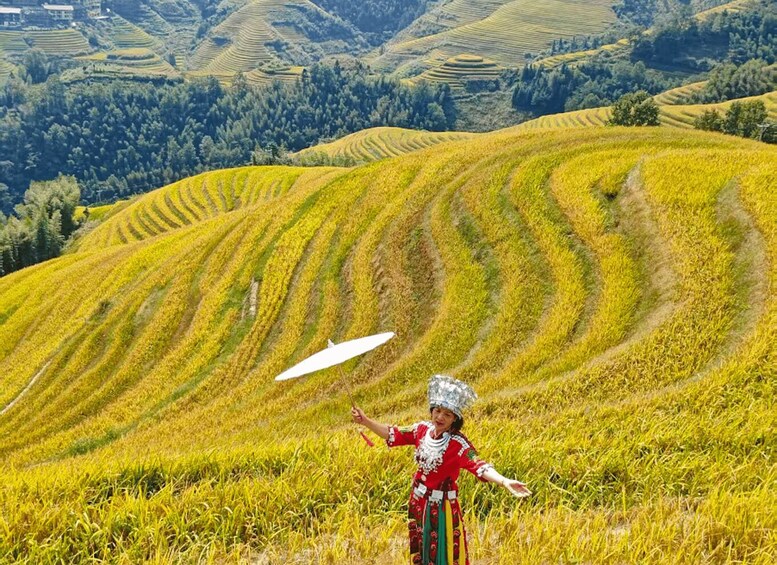 A person in traditional attire standing in a rice paddy field with terraced hills in the background. 1