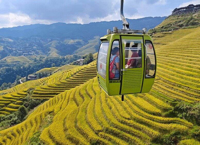 A cable car moving over terraced fields with a mountainous backdrop. 2