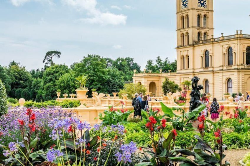 A historic building with a clock tower, surrounded by a well-maintained garden with various flowers and statues. 4