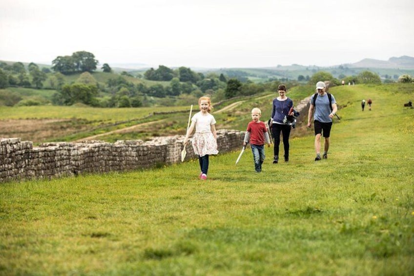 A family walking in a grassy field with stone walls and hills in the background. 5