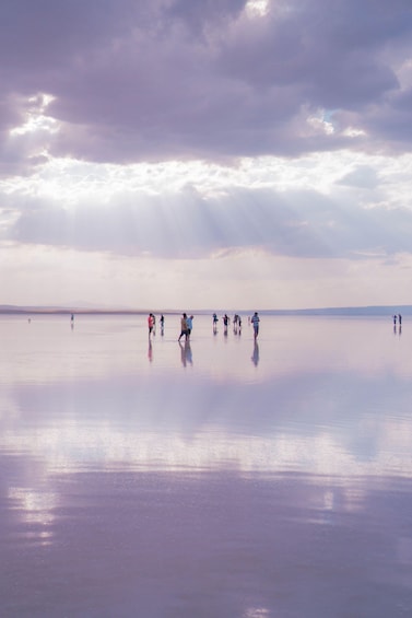 A group of people walking on a calm, reflective water surface with a cloudy sky above. 3