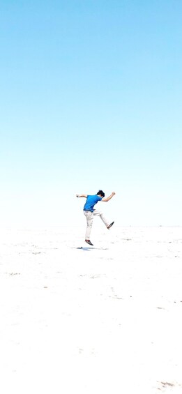 A person jumping in a white, flat landscape under a clear sky. 4