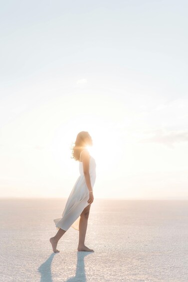 A person in a white dress walking on a beach with the sun low on the horizon. 4